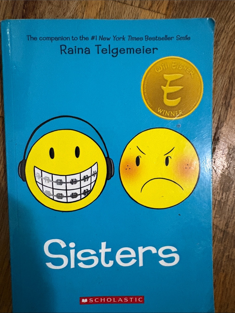 Sisters by Raina Telgemeier — Bright Blue Cover with Yellow Emoji Faces